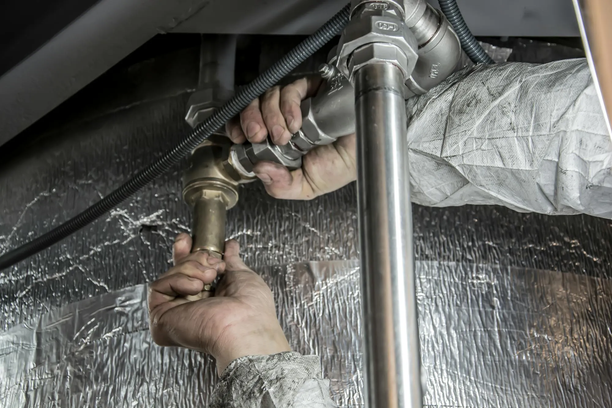 Plumber's hands tightening a brass fitting on copper pipework under a sink